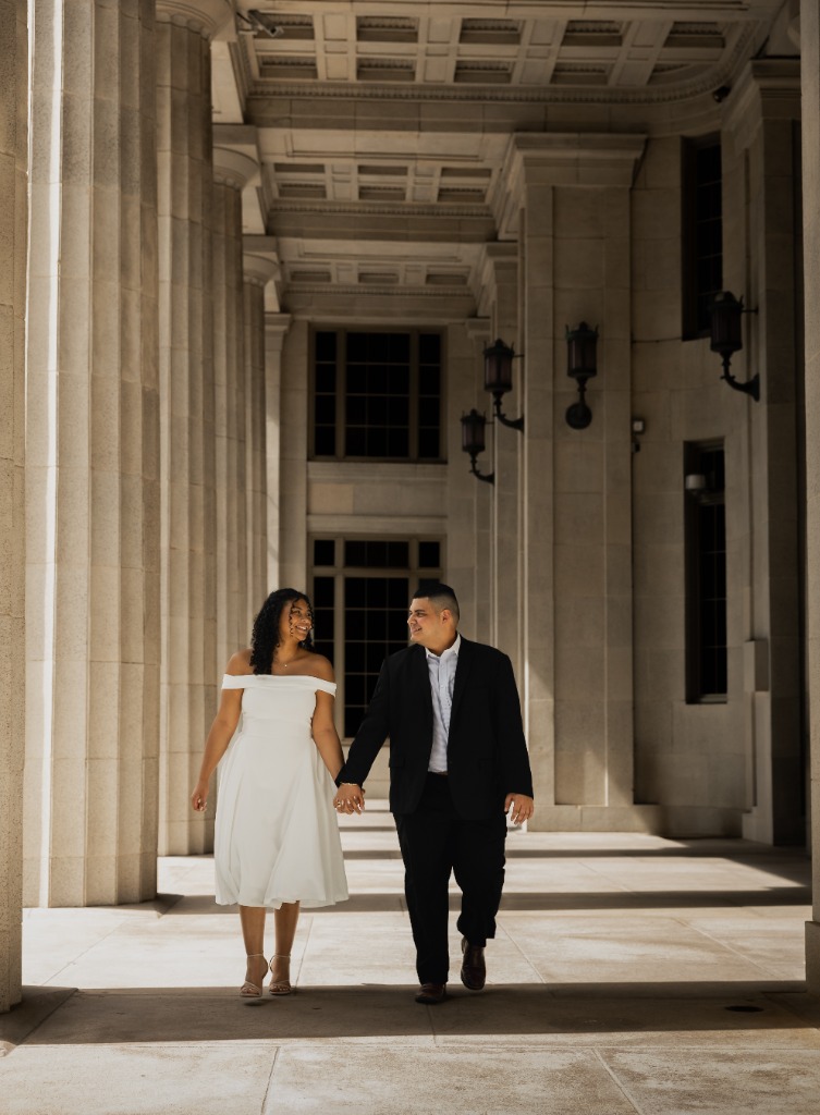 Elegant engagement session with couple walking hand-in-hand between massive stone pillars