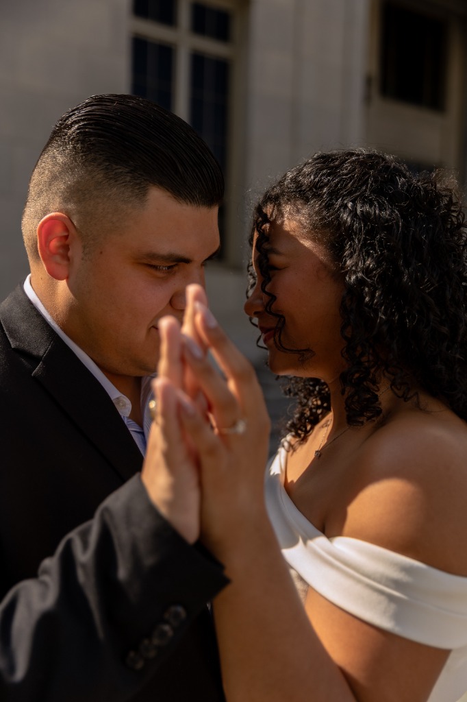 Close-up portrait of the couple's hands intertwined, showcasing the diamond engagement ring in soft lighting