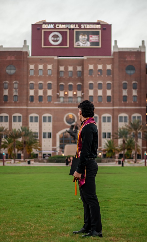 Portrait of graduate in FSU sash standing sideways and looking towards Doak Campbell Stadium