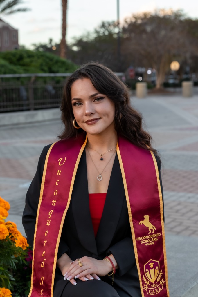 Graduation portrait of a smiling female graduate wearing an Unconquered Scholars Program sash