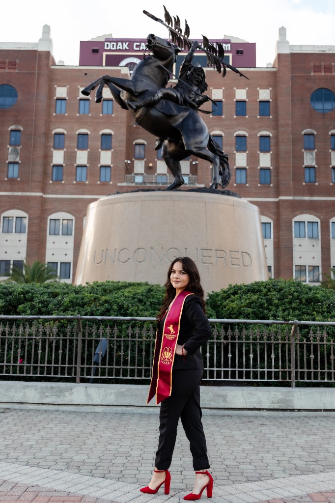 Graduate standing in front of FSU Unconquered statue in black suit and red heels
