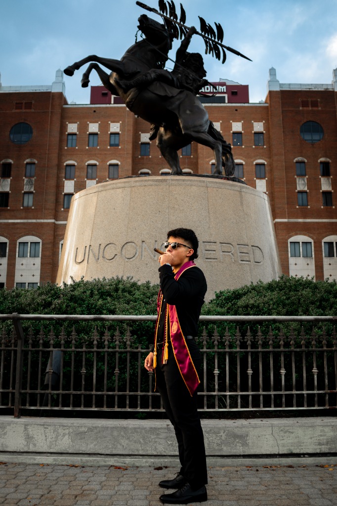 Graduate in front of the FSU Unconquered statue smoking a celebratory cigar