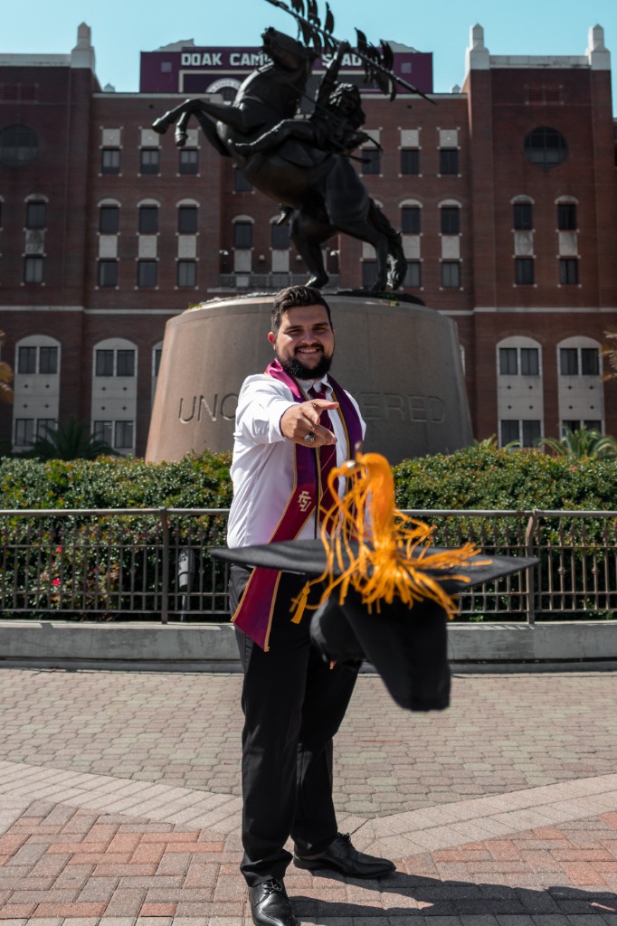 Graduation portrait showing a graduate throwing his cap in front of a campus building