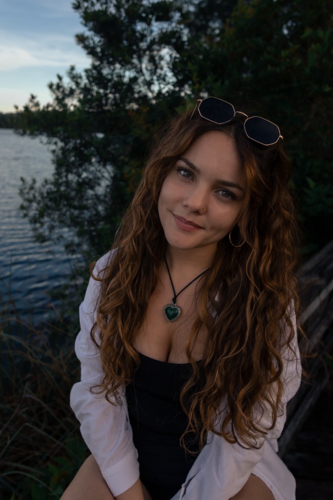 Smiling portrait of a woman with curly hair sitting on a wooden boardwalk by the lake
