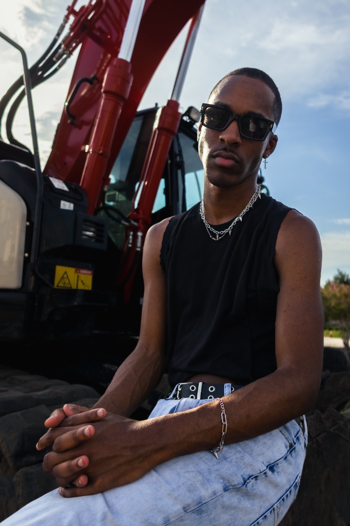Man wearing sunglasses and a black tank top sitting on a red excavator and looking at the camera