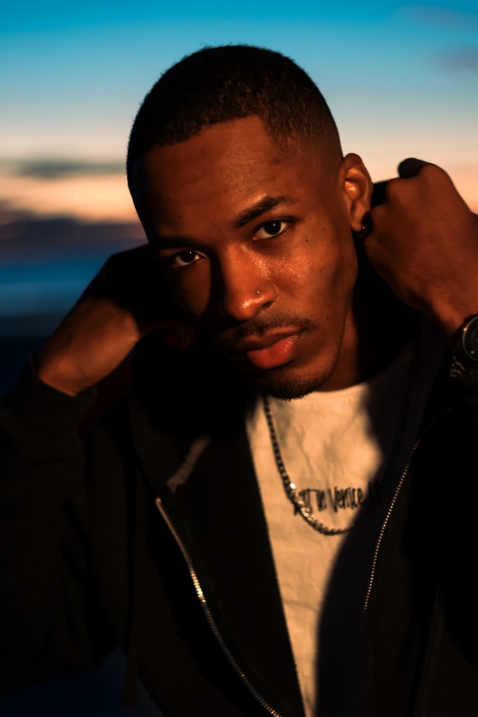 Close-up portrait of a man wearing a black hoodie looking directly at the camera in warm sunset light
