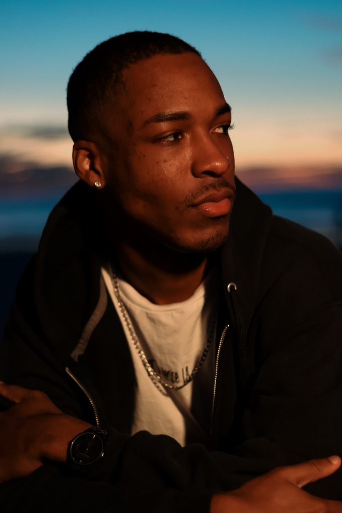 Man wearing a black hoodie looking off into the sunset light in profile view