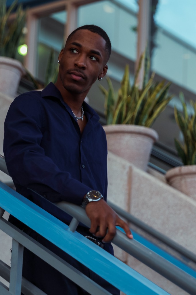 Curated editorial portrait of a man looking to the side on outdoor stairs with potted plants behind him