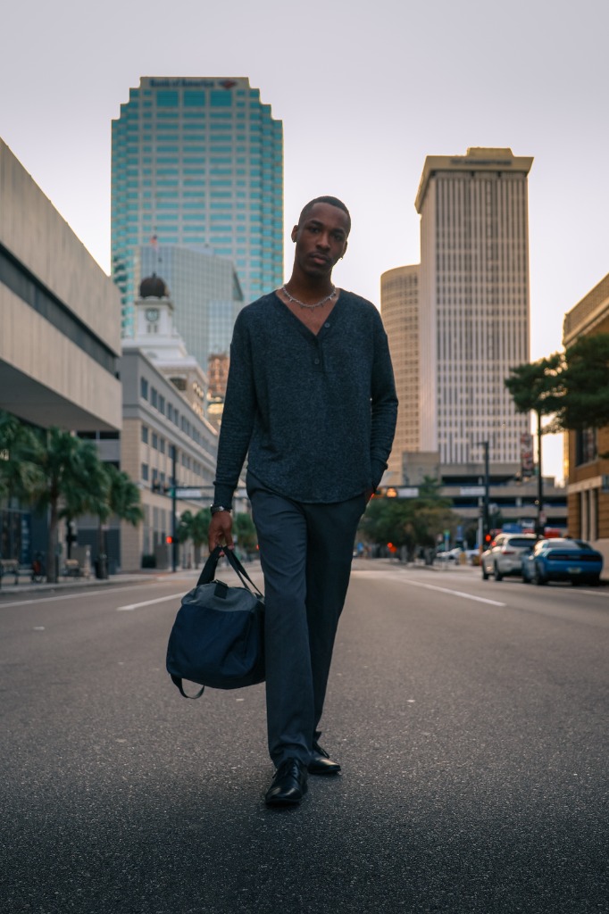 Man with a bag walking down the center of an urban street with city skyscrapers in the background at sunset