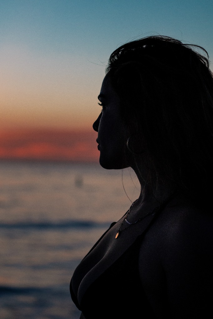 Close-up profile portrait of a woman looking out at the sunset over the sea in soft, warm lighting