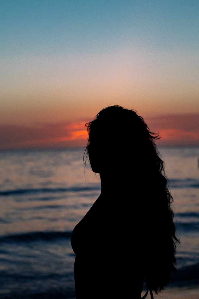 Stunning silhouette portrait of a woman in profile against a vibrant orange sunset sky over the ocean