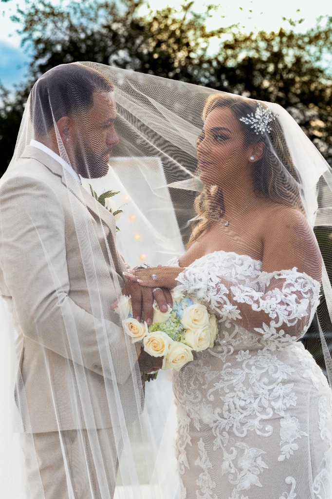 Romantic portrait of bride and groom facing each other closely, covered by the bride's sheer wedding veil